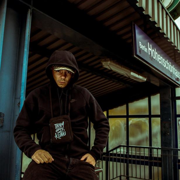 Ein Mann mit Kapuze sitzt am Bahnhof Berlin-Hohenschönhausen.
