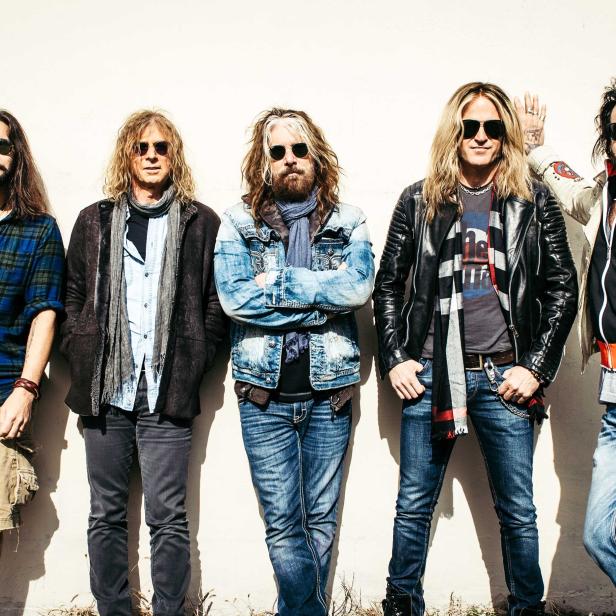 Die Rockband The Dead Daisies posiert vor einer Wand.