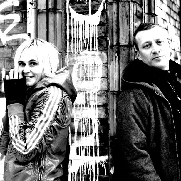 Schwarzweißfoto von zwei Personen vor einer Wand mit Graffiti.