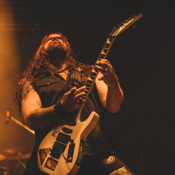 Ein Gitarrist mit langem Haar spielt auf der Bühne E-Gitarre.