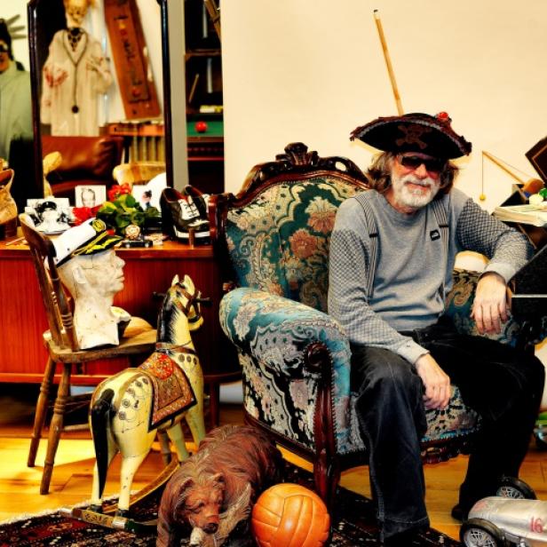 Helge Schneider sitzt mit Piratenhut und Sonnenbrille in einem dekorierten Sessel.
