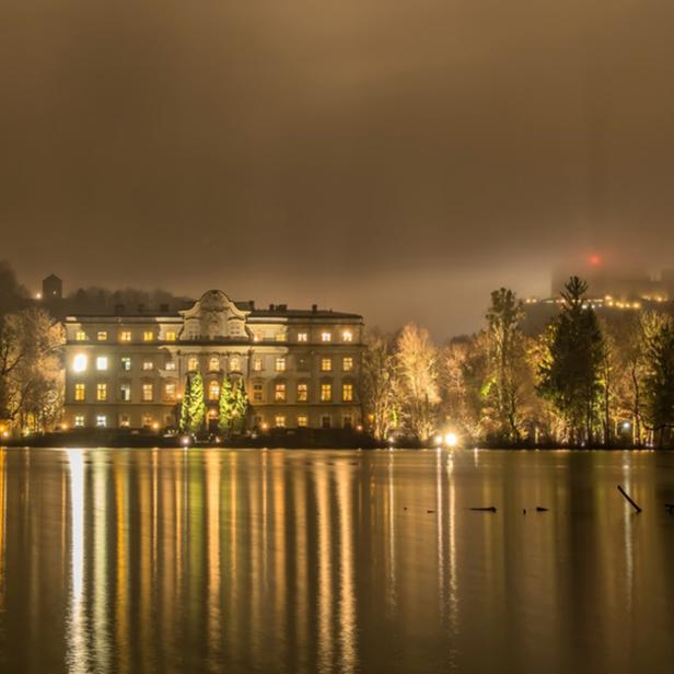Das erleuchtete Schloss Mirabell spiegelt sich im Wasser.