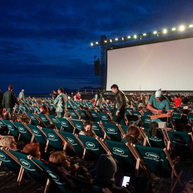 Zuschauer sitzen in Liegestühlen am Strand vor einer großen Leinwand beim Filmfestival in Cannes.