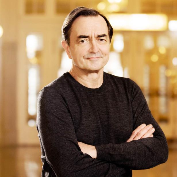 Pierre-Laurent Aimard posiert mit verschränkten Armen vor einem goldenen Hintergrund.