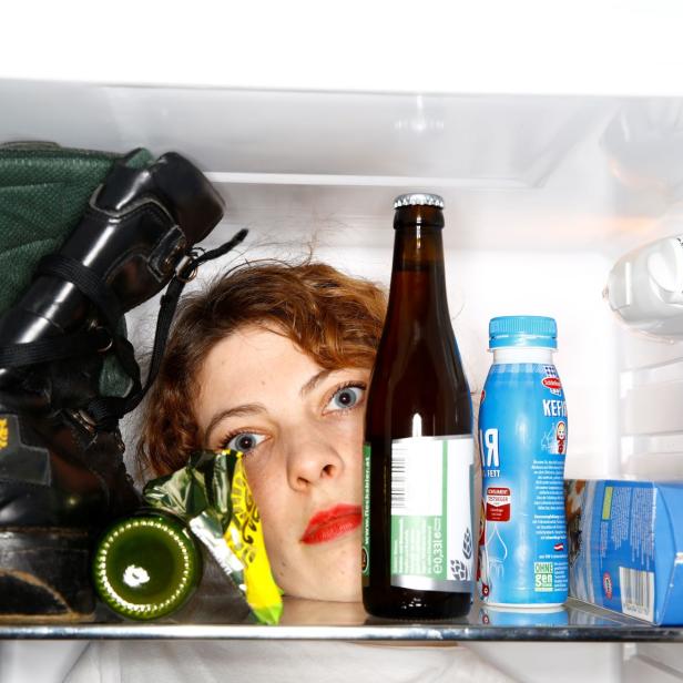 Eine Frau schaut aus einem Kühlschrank voller Stiefel, Bier und Milch.