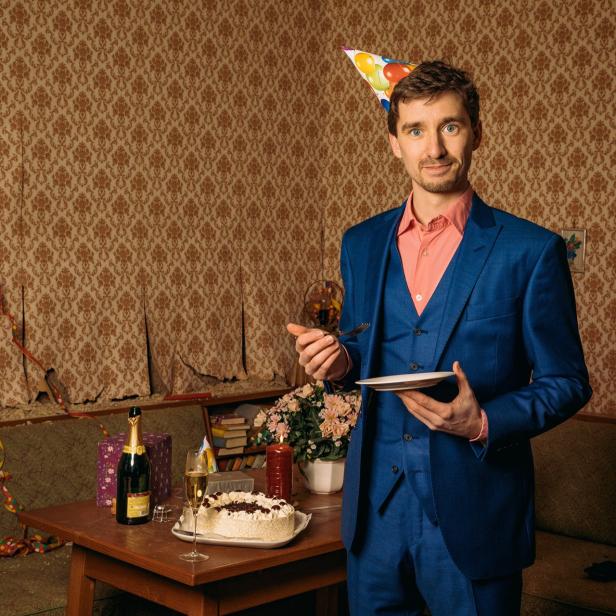 Ein Mann mit Partyhut und Kuchen in einem dekorierten Raum.
