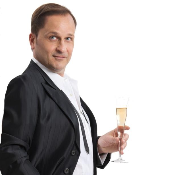 Ein Mann im Anzug hält ein Glas Sekt in der Hand.