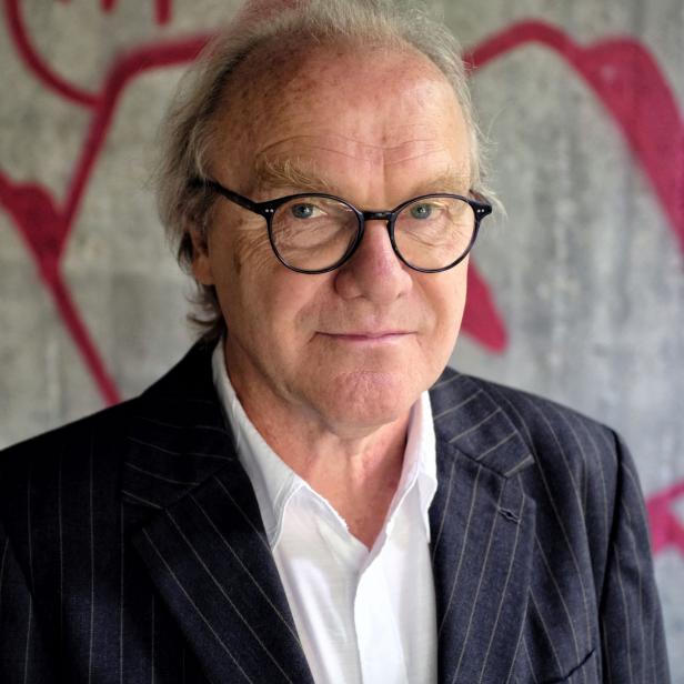 Ein Mann mit Brille und Anzug steht vor einer Wand mit Graffiti.