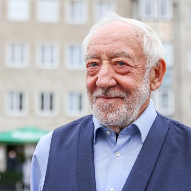 Ein älterer Mann mit Bart und Weste vor einem Gebäude.
