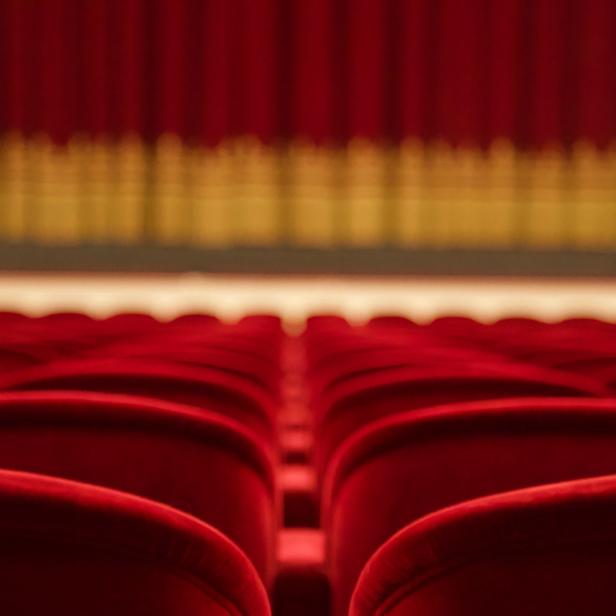 Rote Sitze in einem leeren Theater vor einem roten Vorhang.
