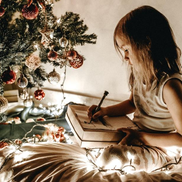 Ein Mädchen sitzt unter einem Weihnachtsbaum und malt in ein Buch.