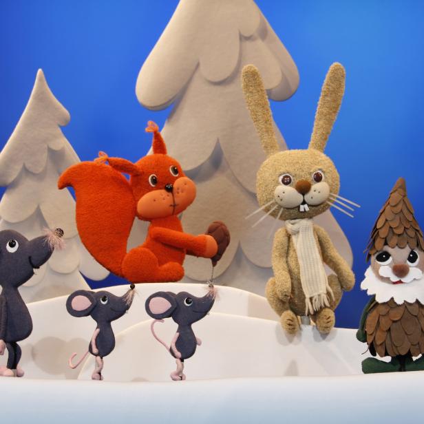 Eine Gruppe von Stofftieren, darunter Eichhörnchen, Hase, Mäuse und ein Zwerg, vor weißen Bäumen.