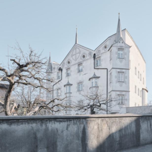 Ein helles Gebäude mit Türmchen und einem Baum im Vordergrund.