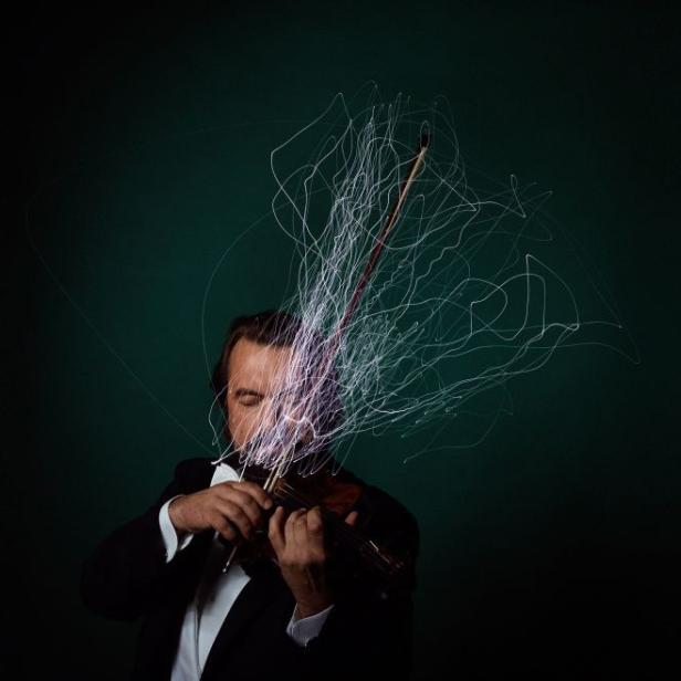Ein Mann im Anzug spielt mit Lichteffekten Violine.
