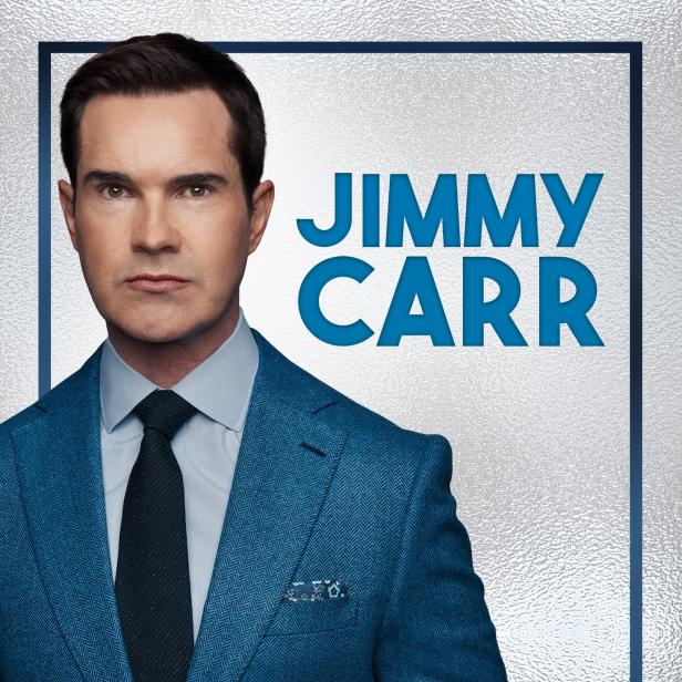 Porträt von Jimmy Carr in einem blauen Anzug vor einem silbernen Hintergrund.