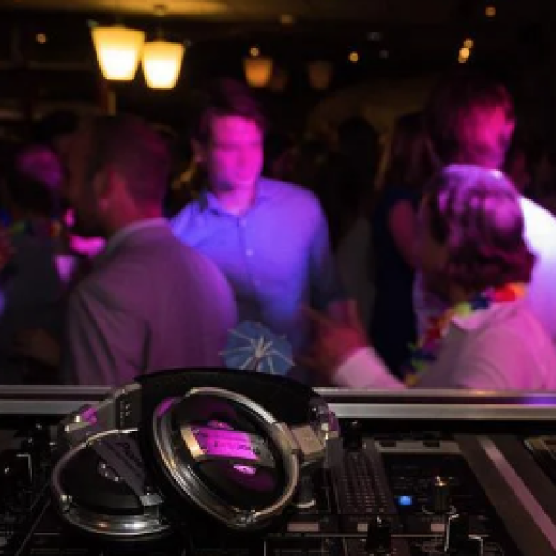 Kopfhörer liegen auf einem DJ-Pult vor einer tanzenden Menschenmenge.