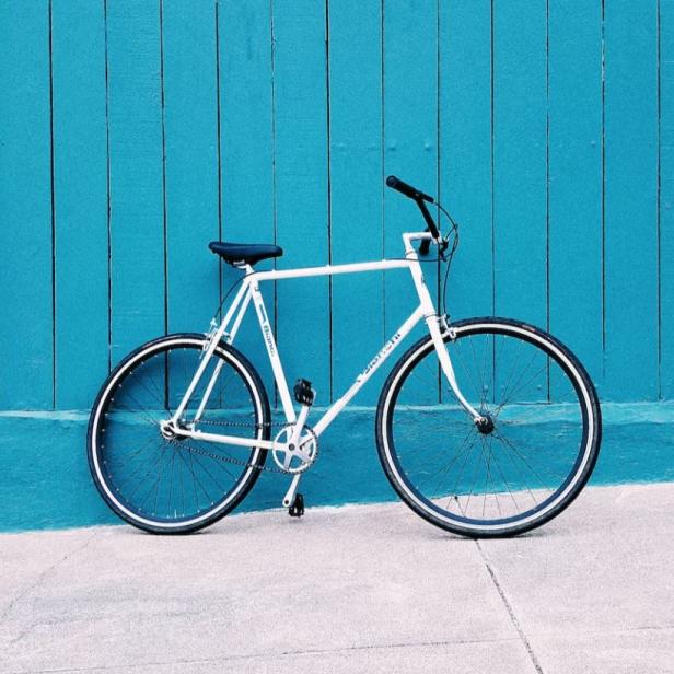 Ein weißes Fahrrad steht vor einer türkisblauen Holzwand.