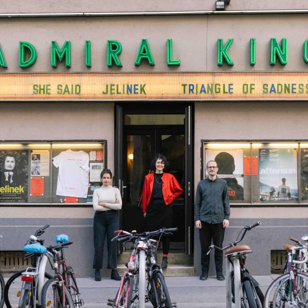Drei Personen stehen vor dem Admiral Kino, dessen Programm „She Said“, „Jelinek“ und „Triangle of Sadness“ umfasst.