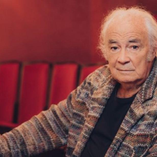 Ein älterer Mann mit weißem Haar sitzt in einem Theatersaal.