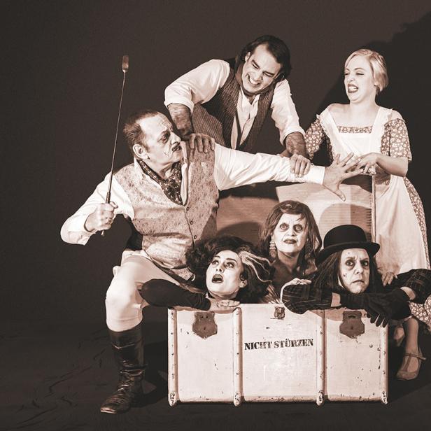 Eine Gruppe von Schauspielern posiert in Kostümen mit einer Requisite, auf der „Nicht stürzen“ steht.