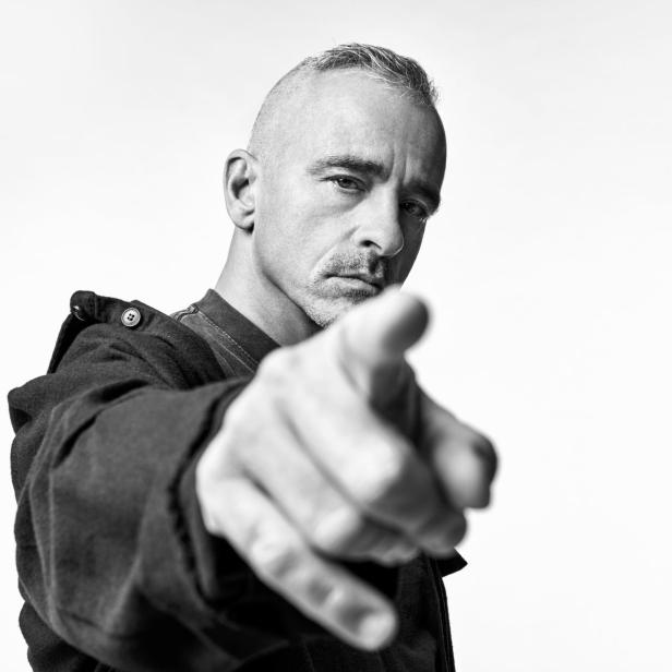 Ein Mann mit grau meliertem Haar und Schnurrbart zeigt mit dem Finger auf den Betrachter.