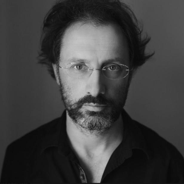 Schwarz-Weiß-Porträt eines Mannes mit Brille und Bart vor einem grauen Hintergrund.