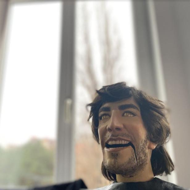 Eine menschliche Puppe mit offenem Mund steht vor einem Fenster.