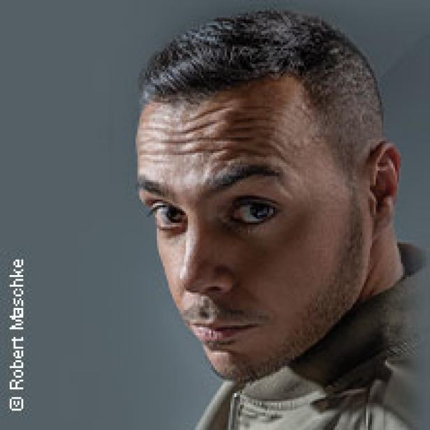 Ein Porträt des deutschen Rappers Samra vor einem grauen Hintergrund.