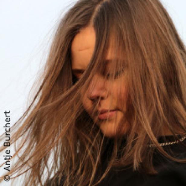 Eine junge Frau mit langen, braunen Haaren blickt nach unten.