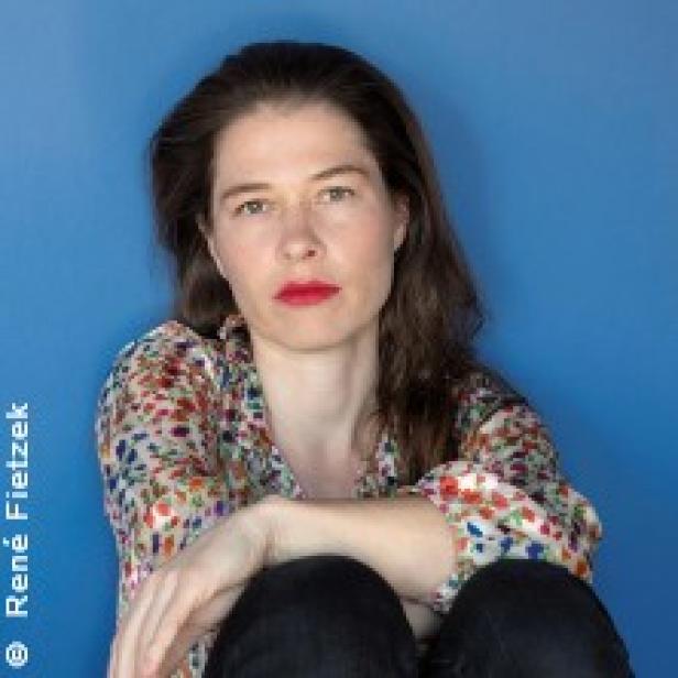 Eine Frau mit roten Lippen sitzt vor einem blauen Hintergrund.
