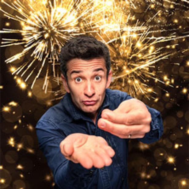 Ein Mann mit offen Händen steht vor einem Hintergrund aus goldenem Feuerwerk.