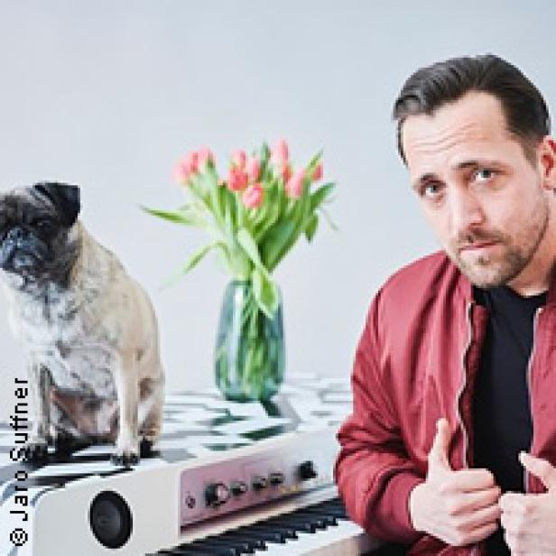 Ein Mann mit Mops und Tulpen sitzt an einem Keyboard und zeigt mit beiden Daumen nach oben.