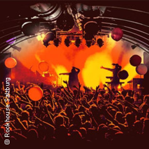 Eine Menschenmenge jubelt bei einem Konzert mit orangefarbener Bühnenbeleuchtung.