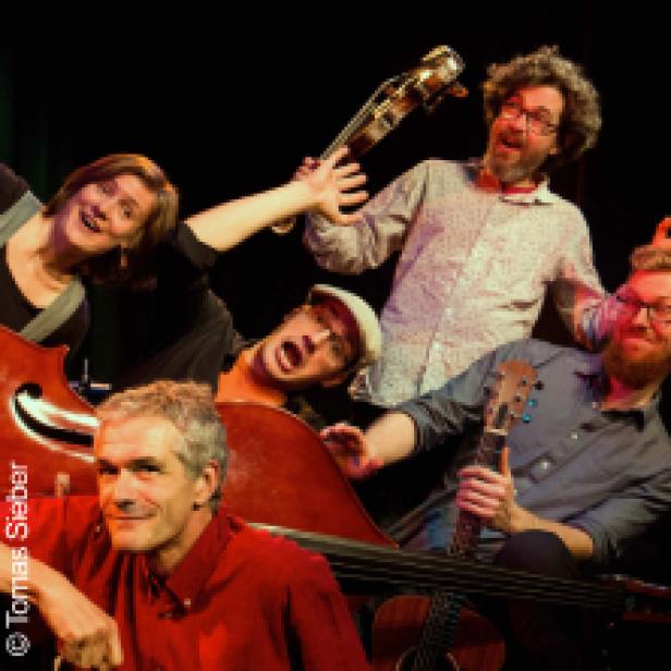 Eine Musikgruppe mit Kontrabässen und Ukulele posiert auf einer Bühne.