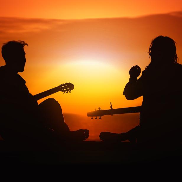 Zwei Personen sitzen mit Gitarren im Sonnenuntergang.
