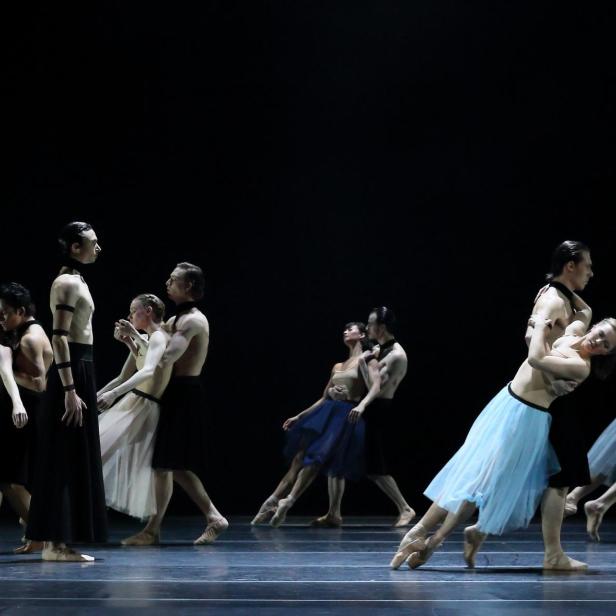 Mehrere Paare tanzen Ballett auf einer dunklen Bühne.