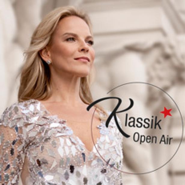Eine blonde Frau im Abendkleid vor einem Gebäude mit der Aufschrift „Klassik Open Air“.