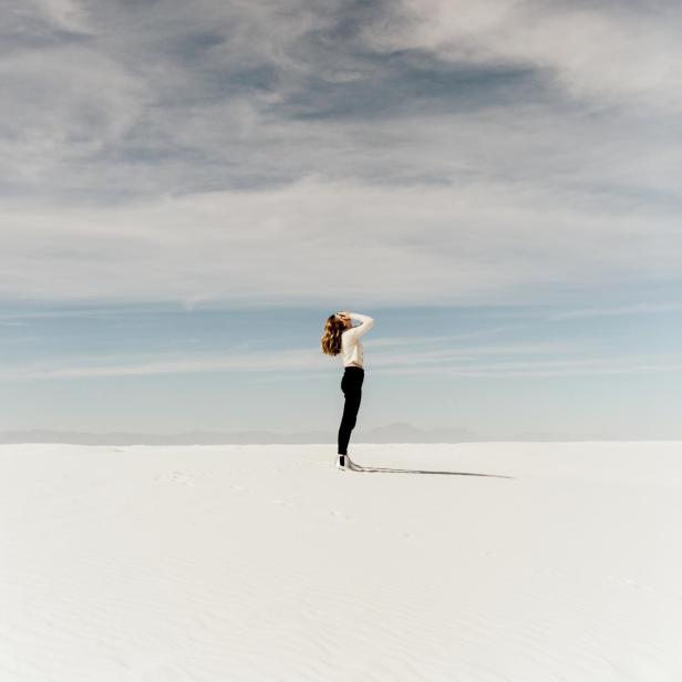 Eine Frau steht in einer weiten, weißen Landschaft und blickt in den Himmel.