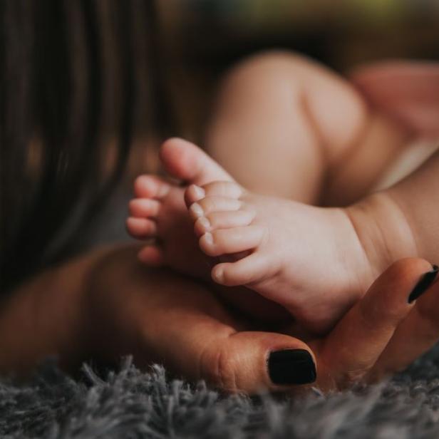 Die Füße eines Babys liegen in der Hand einer Frau.