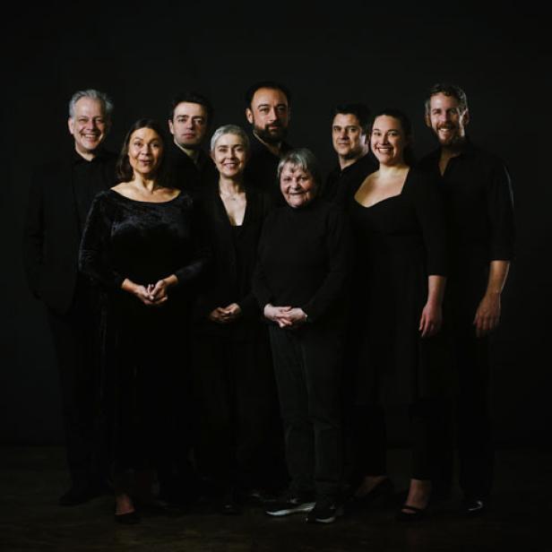 Eine Gruppe von neun Personen posiert vor einem dunklen Hintergrund.