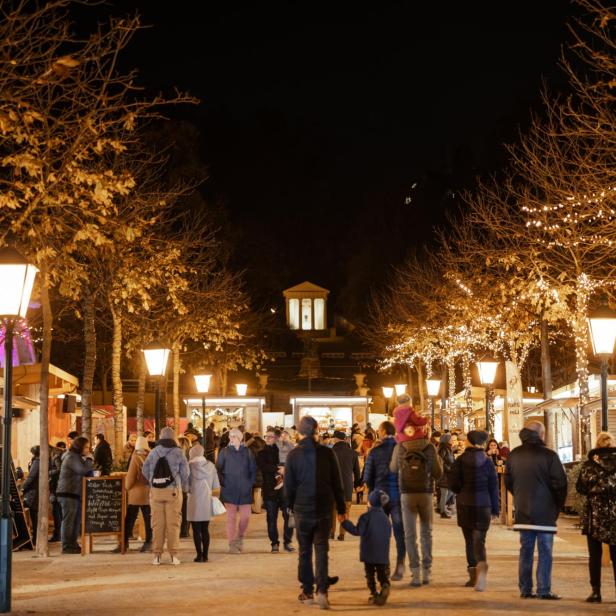 Auf einem Weihnachtsmarkt schlendern Menschen an beleuchteten Ständen vorbei.