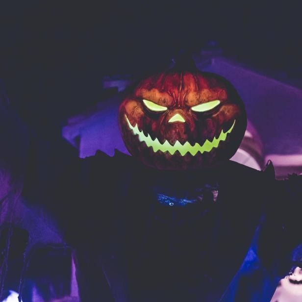 Eine gruselige Halloween-Dekoration mit einem Kürbiskopf und leuchtenden Augen.