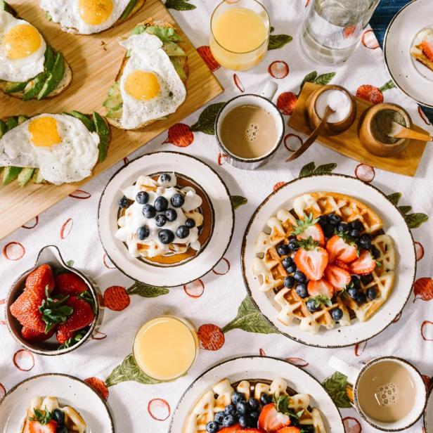 Ein reich gedeckter Frühstückstisch, mit Waffeln, Spiegelei auf Brot, Kaffees und Säften