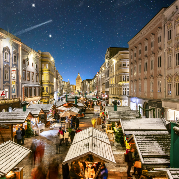 Blick auf einen belebten Weihnachtsmarkt in einer Stadt bei Nacht.