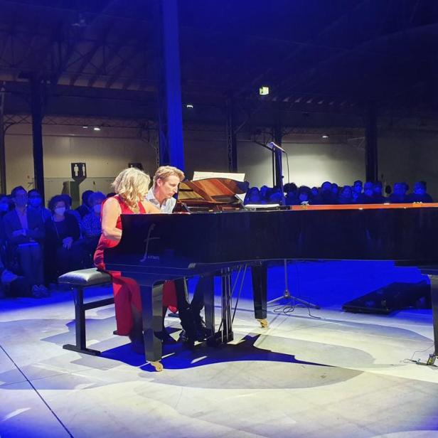 Zwei Pianisten spielen vor Publikum auf einem schwarzen Flügel.