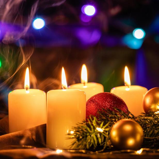 Vier brennende Kerzen stehen neben Weihnachtskugeln und Tannenzweigen.
