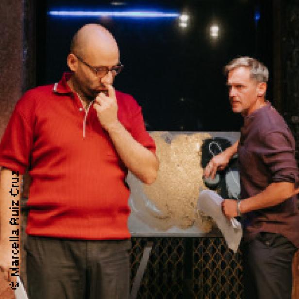 Zwei Männer stehen auf einer Bühne, einer im roten Hemd, der andere im lila Hemd.