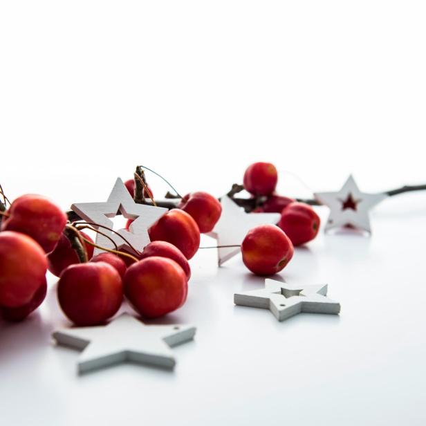 Dekorative rote Zieräpfel und Holzsterne auf einem weißen Untergrund.
