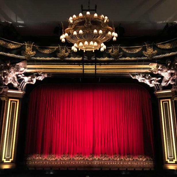 Ein roter Theatervorhang unter einem verzierten Kronleuchter.