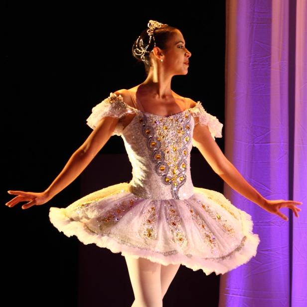 Eine Ballerina in einem weißen Tutu steht auf der Bühne.